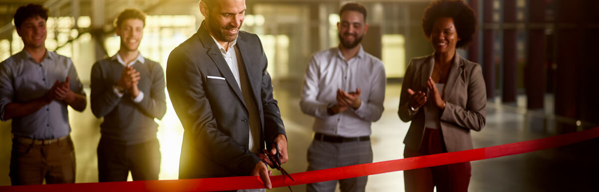 Man cutting ribbon with employees