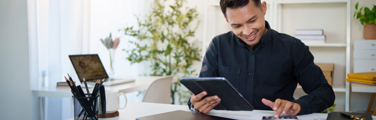 man at desk using calculator and tablet