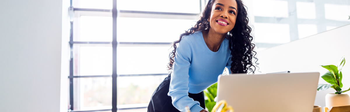 Smiling woman at desk looking up from computer